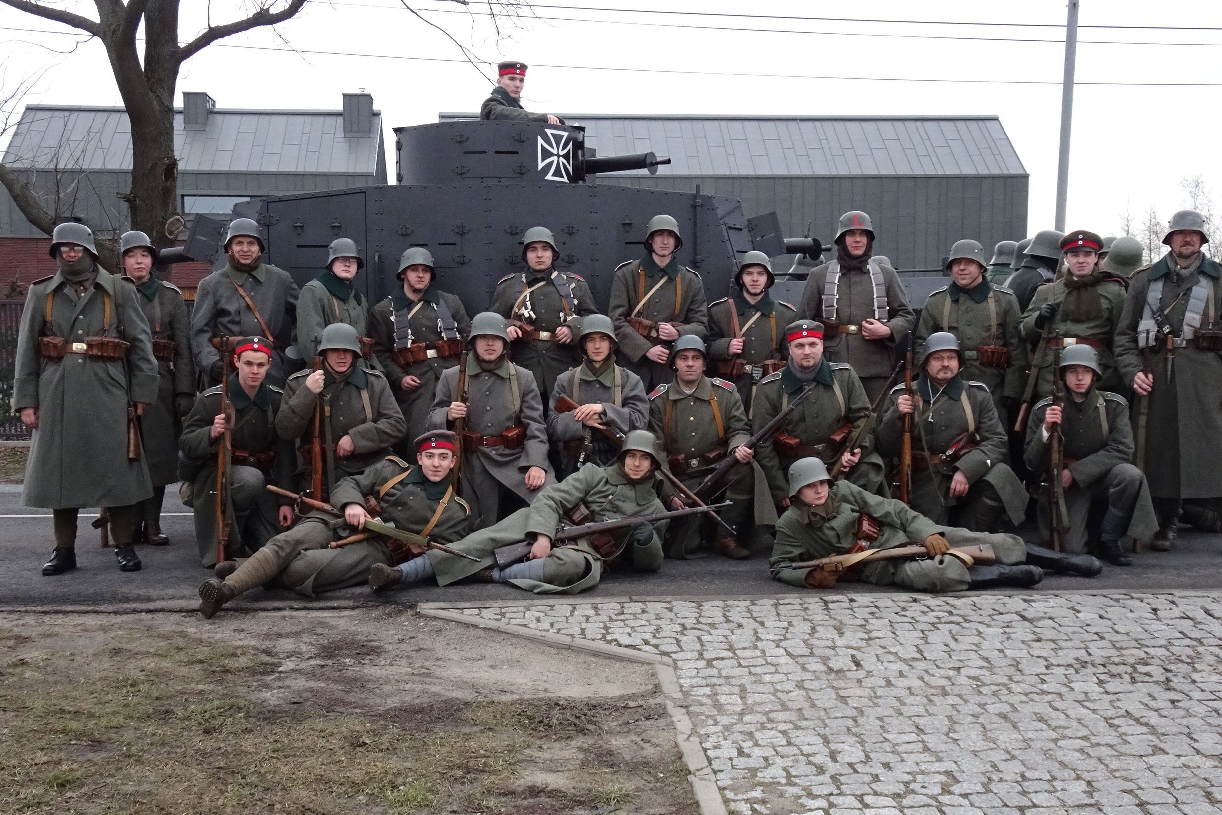 Członkowie grupy rekonstrukcyjnej pozują grupowo do zdjęcia na tle stojącego za nimi samochodu pancernego Erhardt M17.