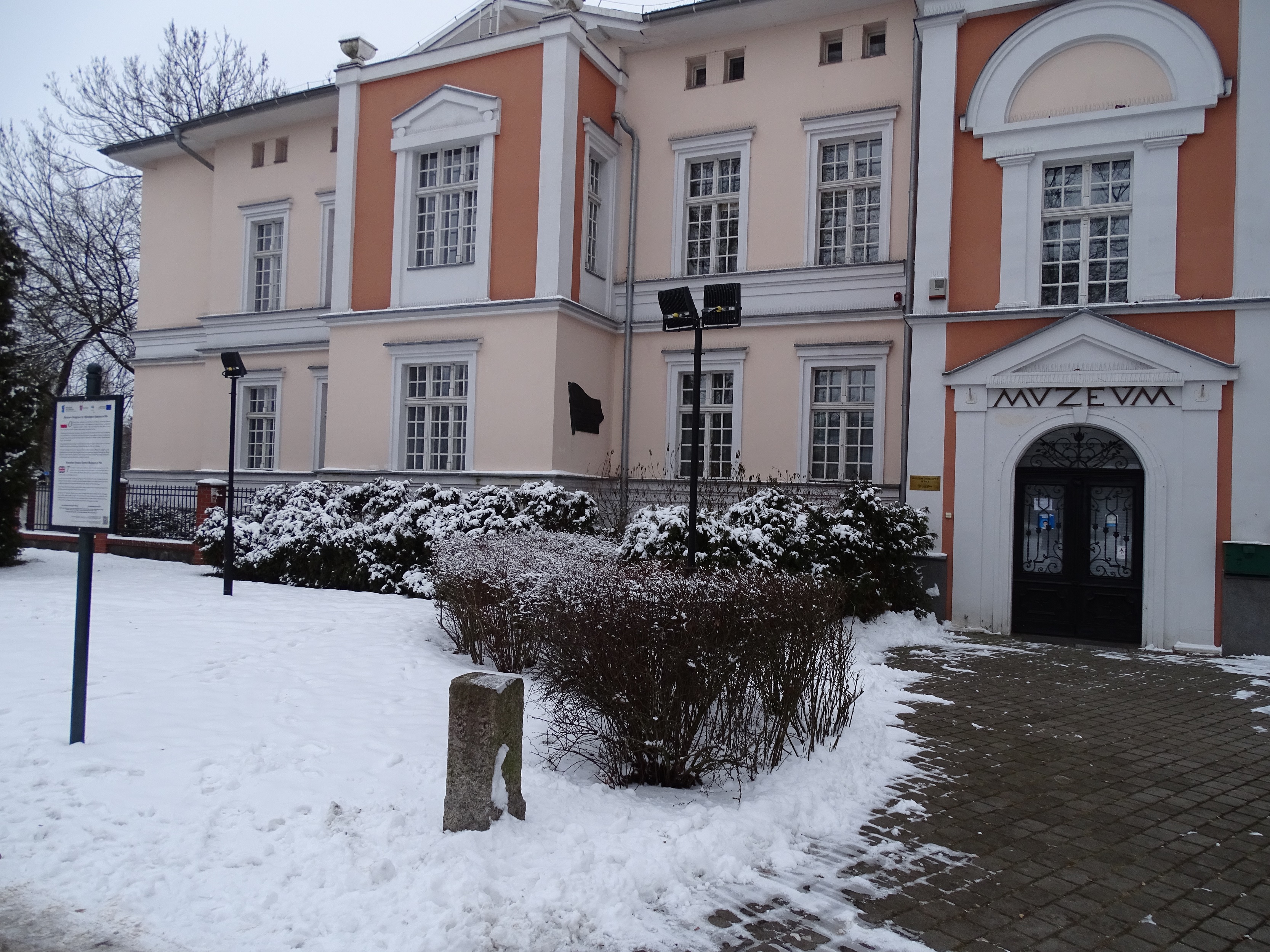 Pośredni kamienny słupek graniczny stojący w śniegu przed budynkiem Muzeum Okręgowego w Pile.