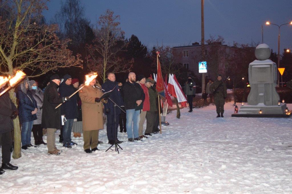 Przemówienie wśród zebranych w towarzystwie flag i pochodni na tle pomnika.