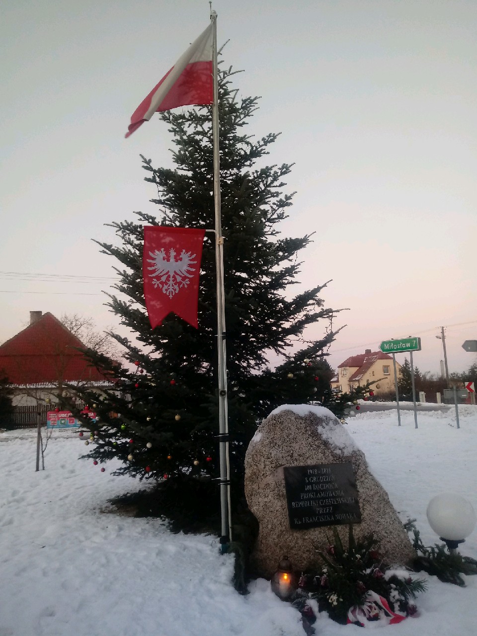 Pomnik obok masztu z flagą Polski i chorągwią powstańczą.