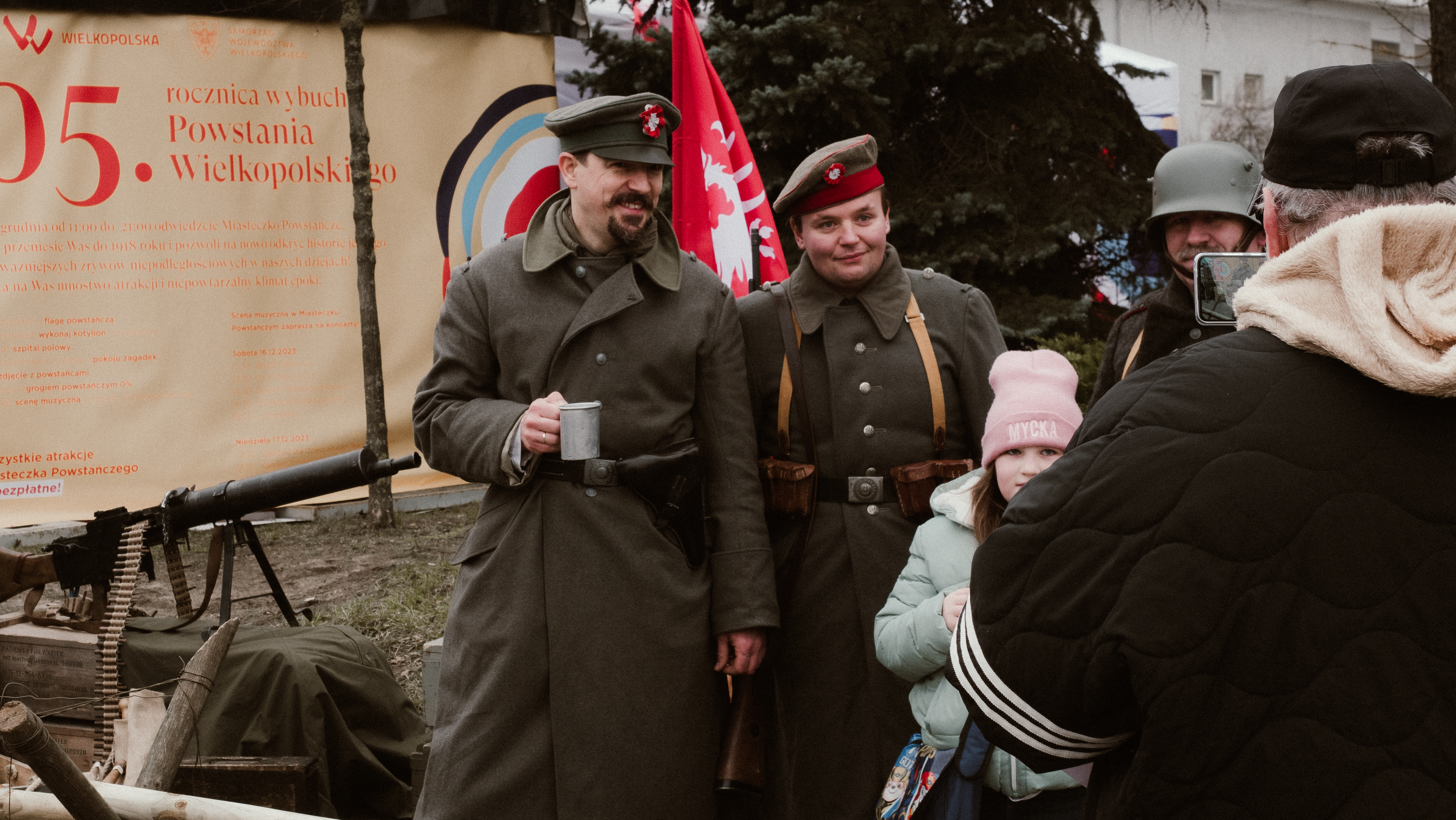 Dwóch mężczyzn w mundurach powstańczych stoi z dziewczynką w różowej czapce i białej kurtce do zdjecia.