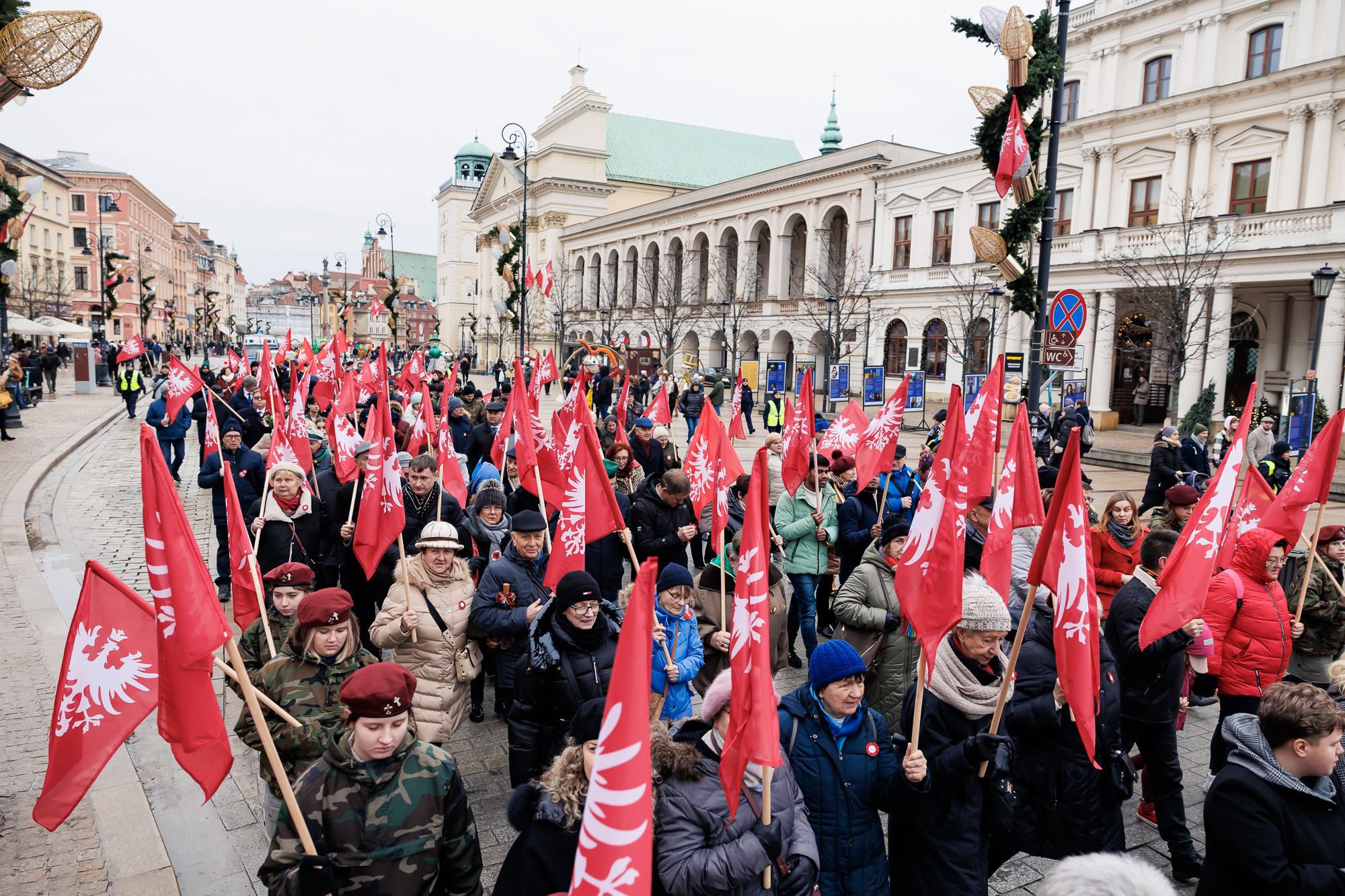 Pochód marszu uczestników uroczystości z powstańczymi flagami na drzewcach.