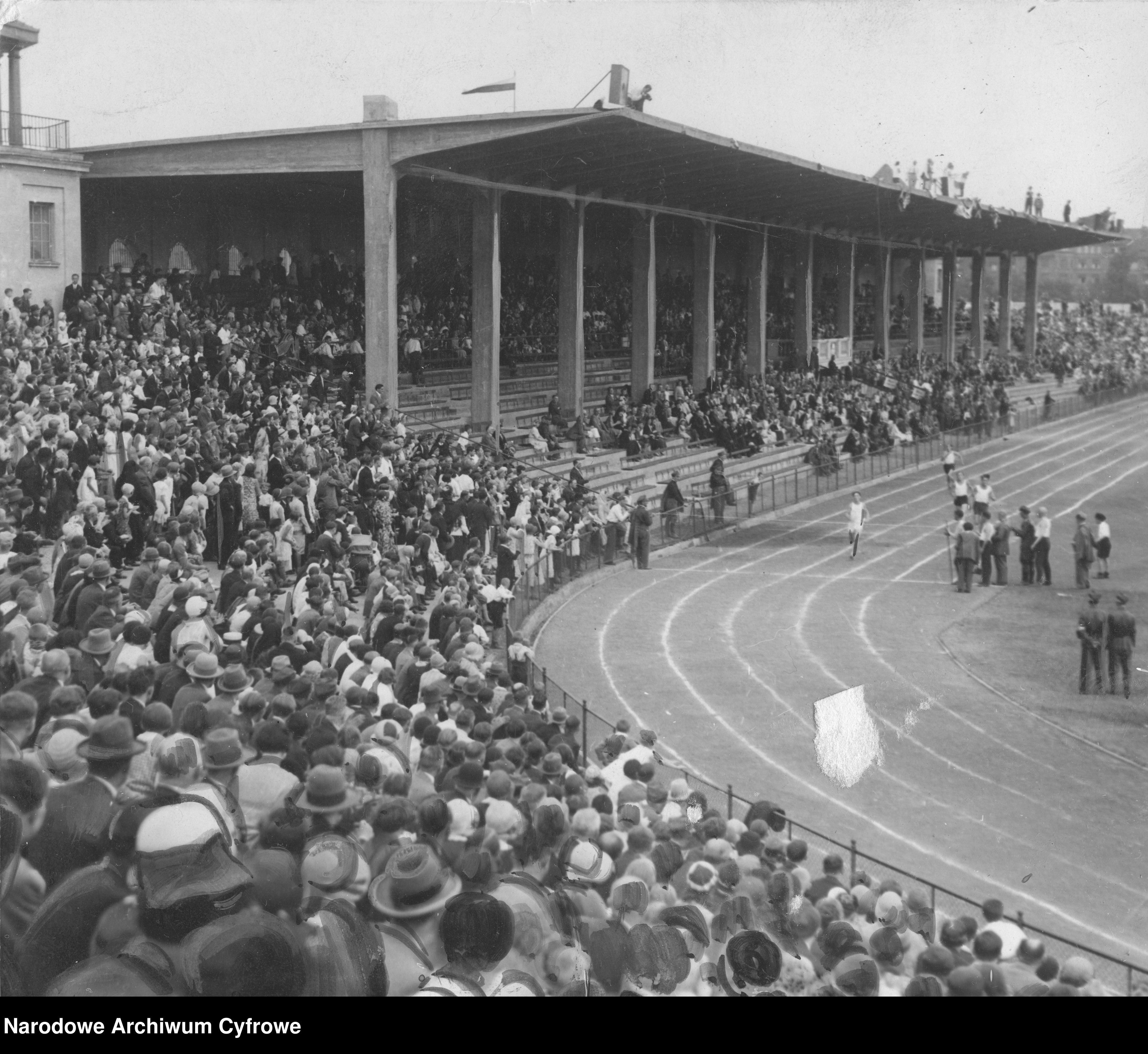 Zawody uczestników zlotu w biegach. Widoczna trybuna stadionu i fragment bieżni z zawodnikami.