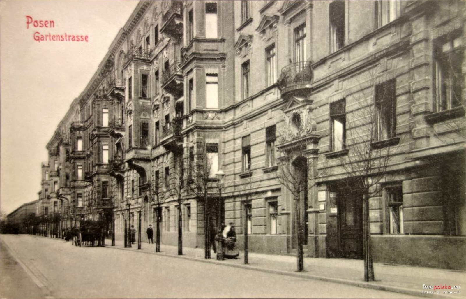 fragment ulicy zabudowanej kamienicami, na chodniku kilka osób, na jezdni powózka, między jezdnią, a chodnikiem rosną drzewa