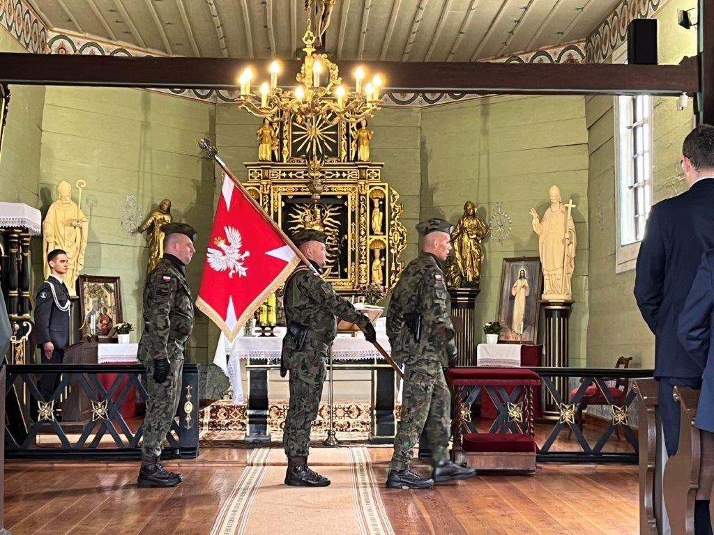 Trzech mężczyzn w mundurach z flagą, w tle ołtarz w Kościele.