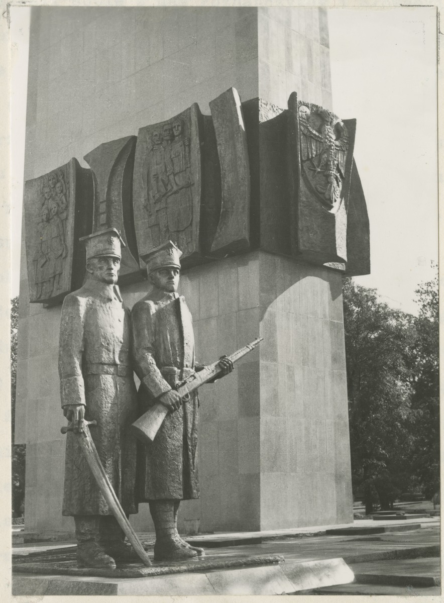 Pomnik, na pierwszym planie dwie rzeźby postaci w mundurach, na drugim planie płaskorzeźba orła