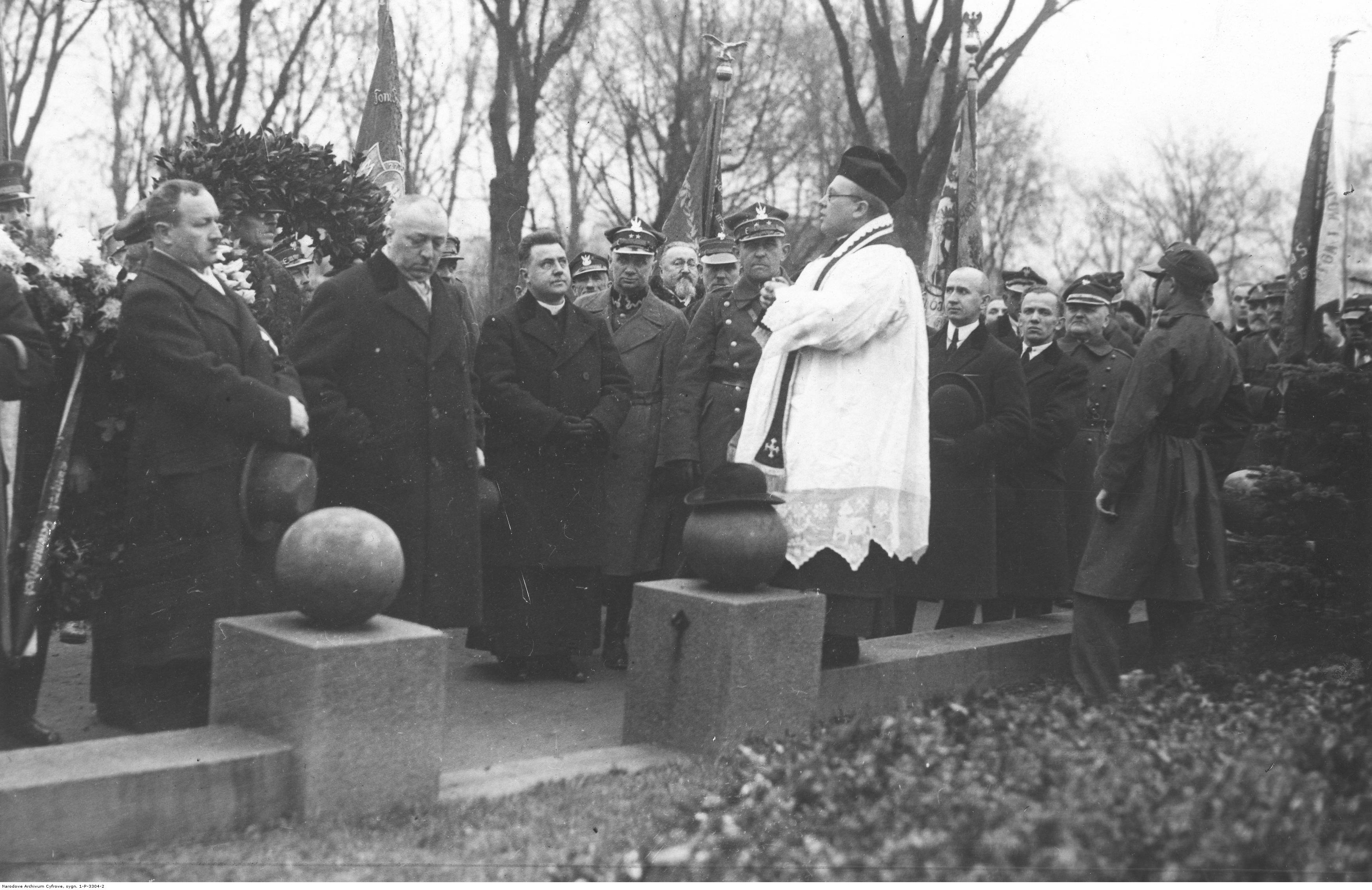 Duchowny przemawia do zgromadzonych mężczyzn, w tle poczty sztandarowe