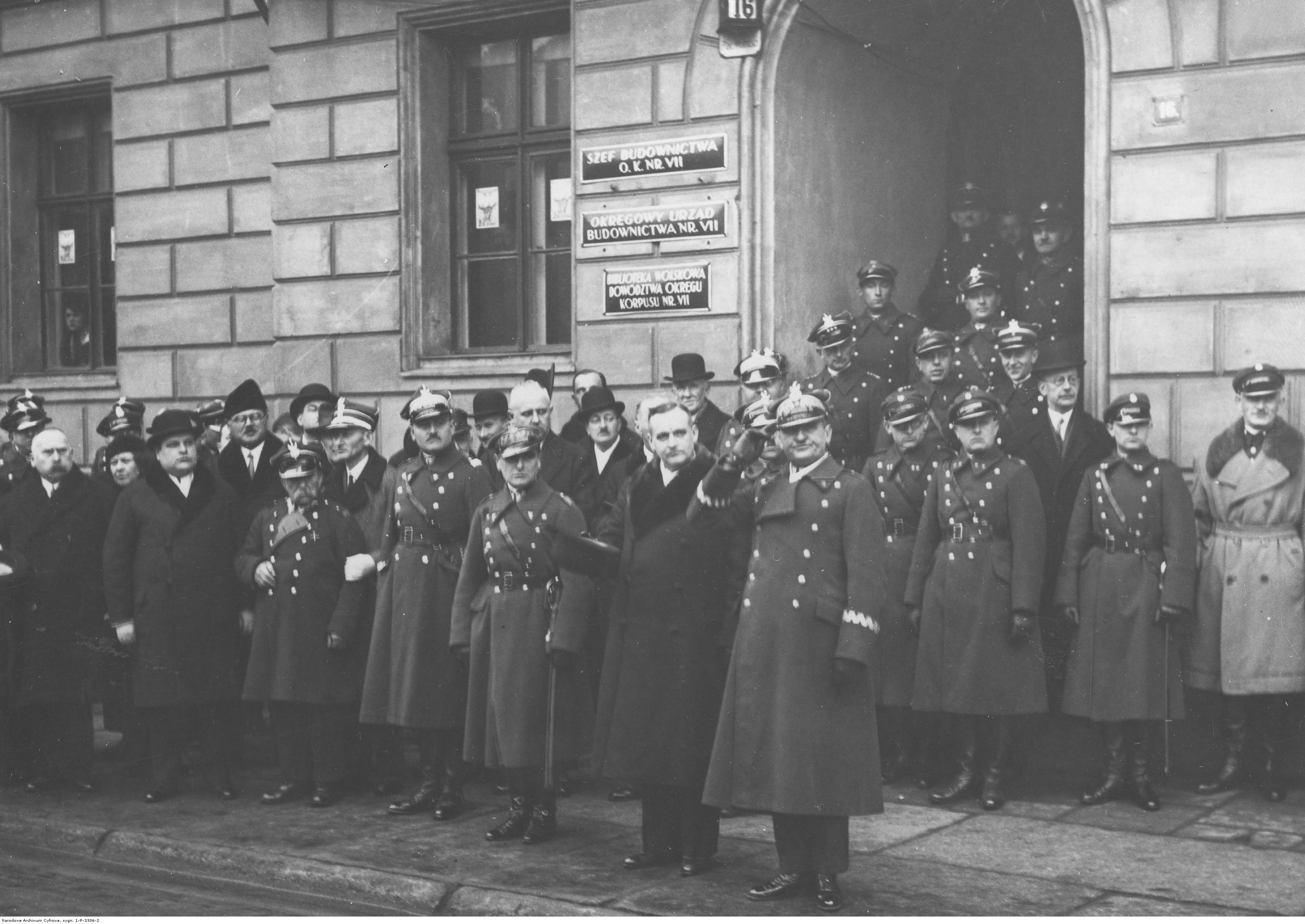 Grupa mężczyzn przed budynkiem, wielu z nich w mundurach wojskowych.