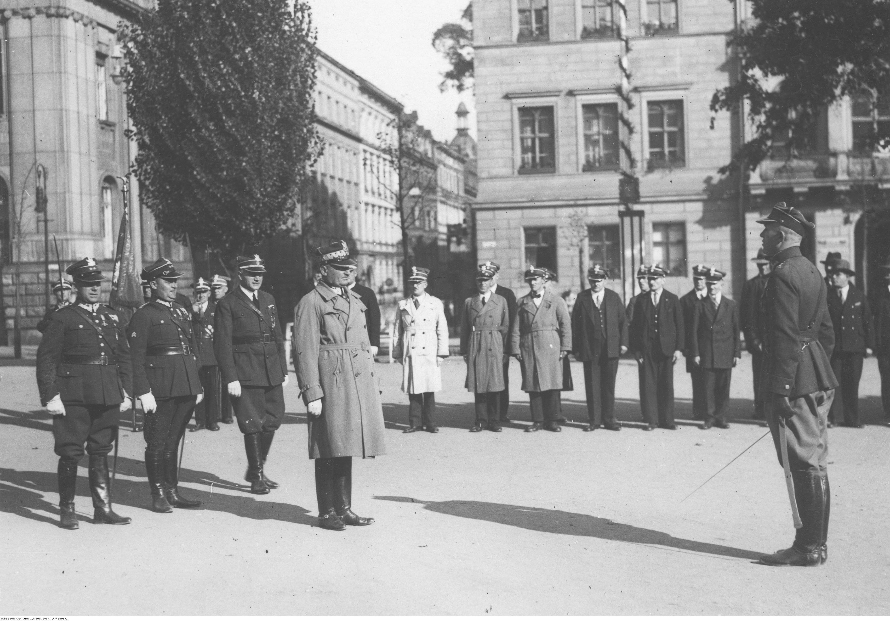 Grupa mężczyzn w mundurach, na pierwszym planie dwójka mężczyzn stojąca na baczność.